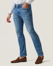 Person wearing blue jeans and brown shoes on a plain background