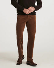 A man modeling a dark brown crewneck sweater and brown corduroy trousers with brown leather shoes, wearing black sunglasses, against a light gray studio background.