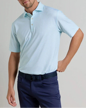 Man wearing a light blue polo shirt and navy pants against a plain background