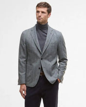 Man wearing a gray blazer, black turtleneck, and dark pants on a white background