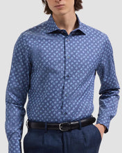 Man wearing a blue patterned shirt and dark pants on a light gray background