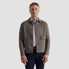 Man wearing a brown jacket over a shirt with a light gray background