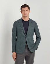 Man wearing a green blazer over a dark shirt and gray pants on a light gray background