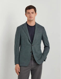 Man wearing a green blazer over a dark shirt and gray pants on a light gray background
