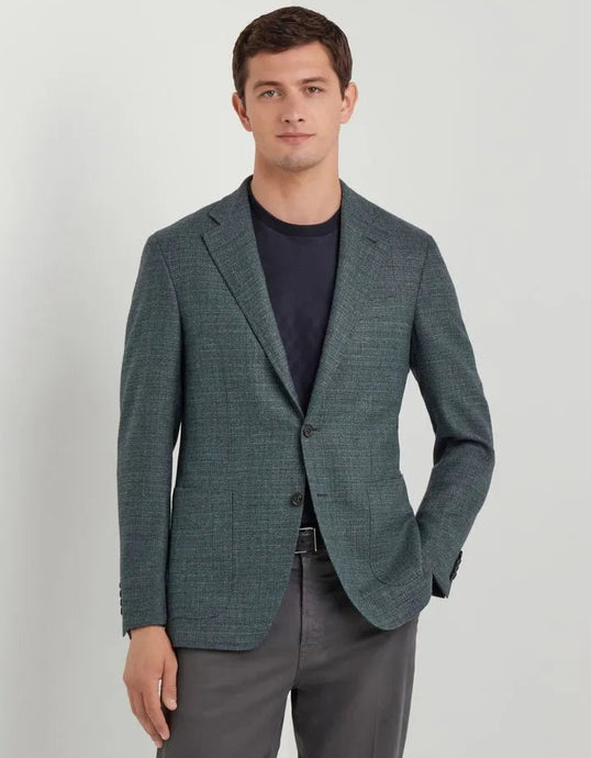 Man wearing a green blazer over a dark shirt and gray pants on a light gray background