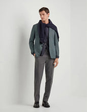 Man wearing a green blazer, gray pants, and a dark scarf on a white background