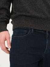 Person wearing a dark gray sweater and blue jeans on a light background