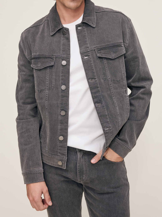 Person wearing a gray denim jacket over a white shirt on a beige background