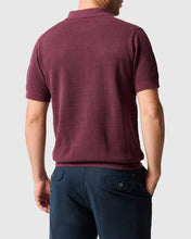 Man wearing a maroon polo shirt and navy pants on a light gray background