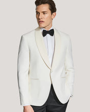 Man wearing a white tuxedo with a black bow tie on a light gray background