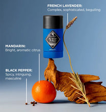 Blue cylindrical product with black cap on a wooden hand holding an orange and lavender sprig against a blue background.