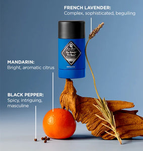 Blue cylindrical product with black cap on a wooden hand holding an orange and lavender sprig against a blue background.