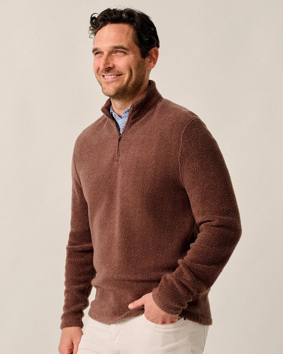 Man wearing a brown sweater and white pants against a plain background