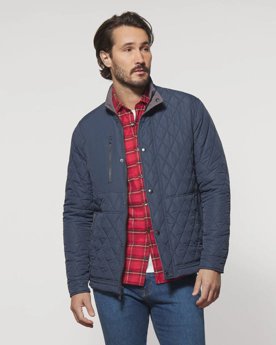 Man wearing a blue quilted jacket over a red plaid shirt on a white background