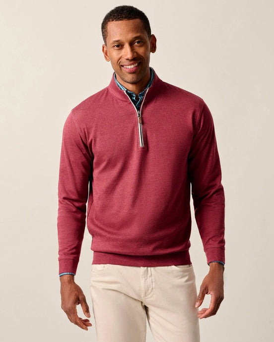 Man wearing a red quarter-zip sweater and white pants on a beige background