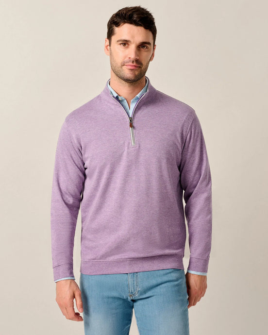 Man wearing a purple quarter-zip sweater and light blue jeans against a beige background