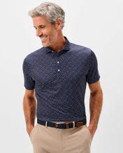 Man wearing a navy polo shirt with a subtle pattern and beige pants on a light gray background
