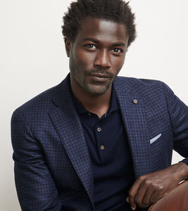 Man wearing a blue checkered blazer over a dark shirt against a plain background