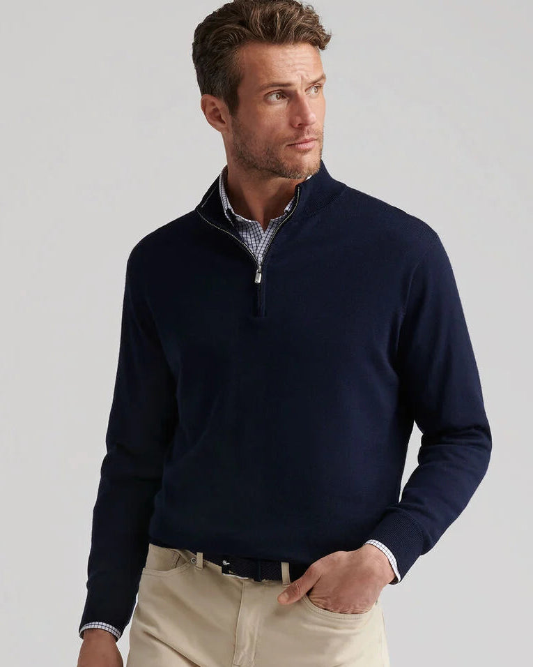 Man wearing a navy half-zip sweater with beige pants on a light gray background