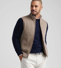 Man wearing a beige vest over a dark shirt with a light background