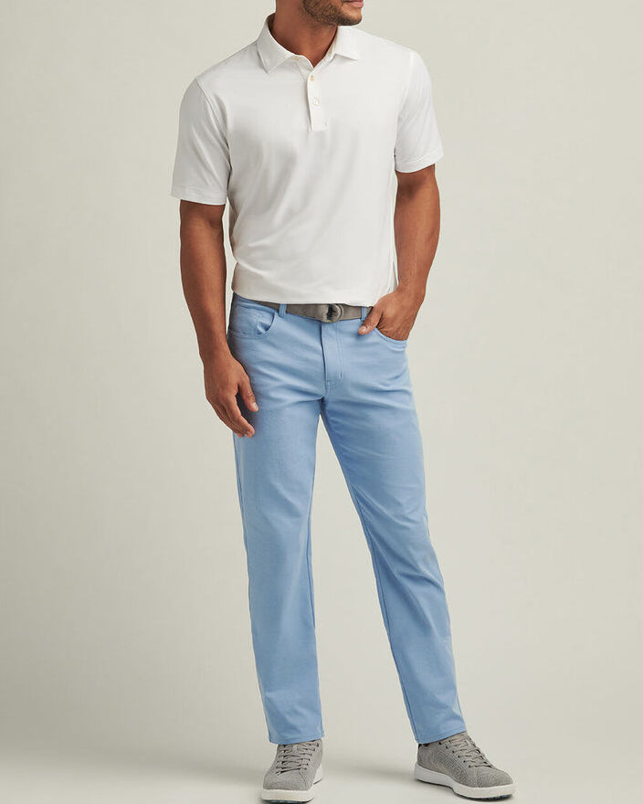 Man wearing a white polo shirt and light blue pants on a beige background