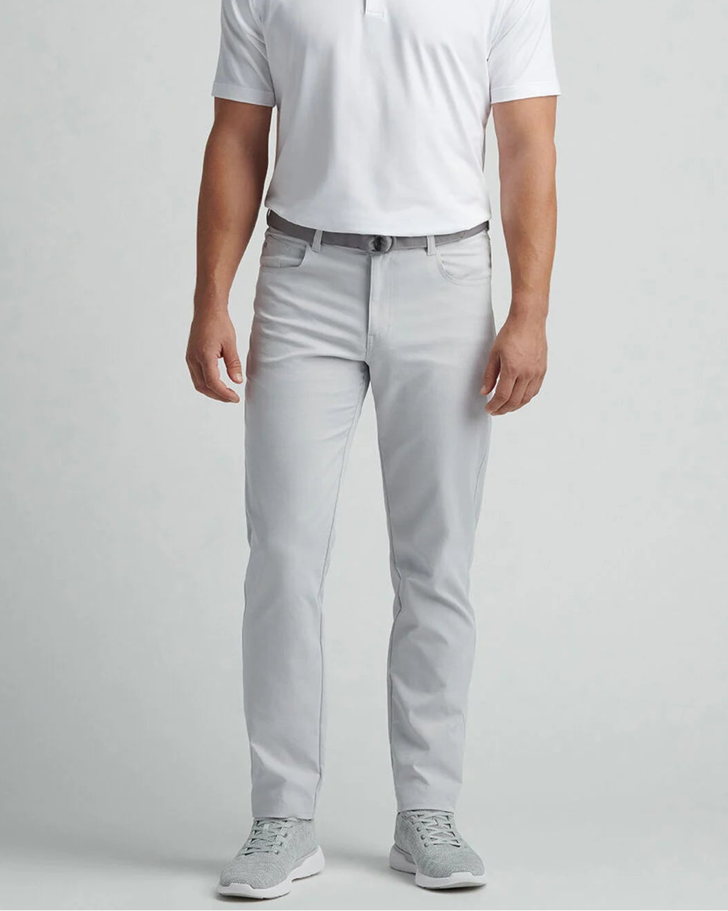 Man wearing a white polo shirt and light gray pants on a plain background
