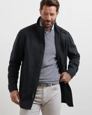 Man wearing a dark jacket over a gray sweater and light pants on a white background