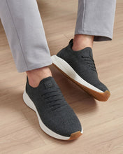 Dark gray sneakers with white soles and brown accents worn on a wooden floor.