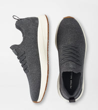 Two dark gray knit slip-on sneakers shown from the side and top views on a light gray background. The shoes feature a thick white midsole with a brown gum outsole and a black interior with 'PETER MILLAR' branding.