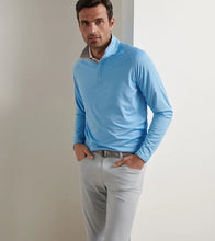 Man wearing a light blue long-sleeve shirt and gray pants against a neutral background