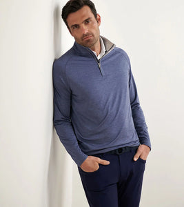 Man wearing a blue long-sleeve shirt leaning against a white wall.