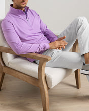 Man sitting on a chair wearing a purple shirt and light gray pants.