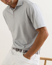 Man wearing a gray striped polo shirt and white pants on a light background
