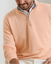 Man wearing a peach-colored quarter-zip sweater against a plain background