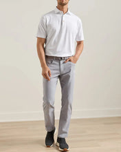 Man wearing a white polo shirt and light gray pants standing against a plain background