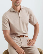 Man wearing a beige polo shirt and pants sitting on a chair against a white background