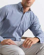 Man wearing a blue and white checkered shirt sitting on a chair.