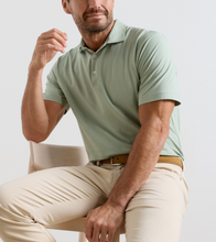 Man wearing a light green polo shirt and beige pants sitting on a chair.
