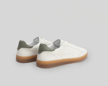 Pair of white sneakers with green soles on a light gray background