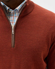 Close-up of a man wearing a rust-colored ribbed quarter-zip sweater over a blue, white, and red plaid collared shirt.