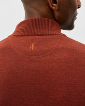 Close-up back view of a man wearing a rust-colored ribbed knit mock neck sweater, showing a small embroidered logo on the upper back.