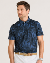 Man wearing a blue patterned polo shirt with white pants on a light background