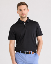 Man wearing a black polo shirt and light blue pants on a gray background