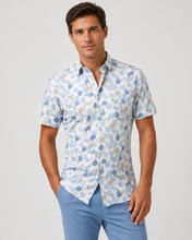Man wearing a short-sleeve patterned shirt and light blue pants on a plain background