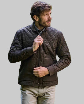 Man wearing a brown quilted jacket standing outdoors with greenery in the background