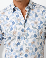 Man wearing a short-sleeve floral shirt and light blue pants against a white background